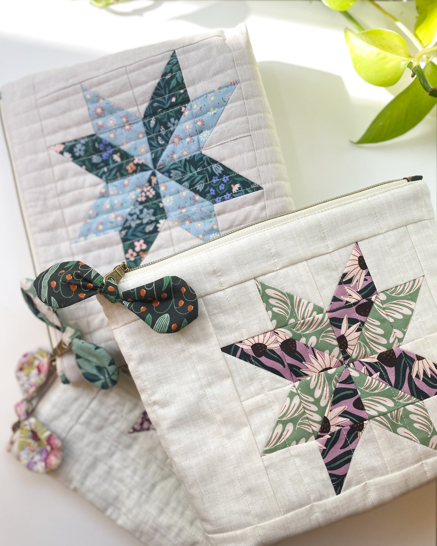 Three zipper pouches made from the same sewing pattern, laid flat and slightly overlapping on a white table. Each pouch features a different fabric design.