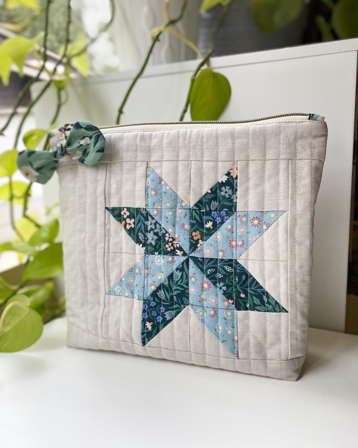 Zipper pouch made from PDF sewing pattern, featuring blue and green Cloud9 organic floral fabric and flat-bottom design, standing on a white table with greenery behind