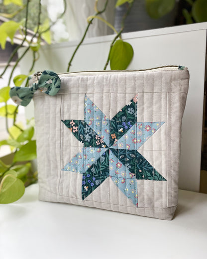Zipper pouch made from PDF sewing pattern, featuring blue and green Cloud9 organic floral fabric and flat-bottom design, standing on a white table with greenery behind