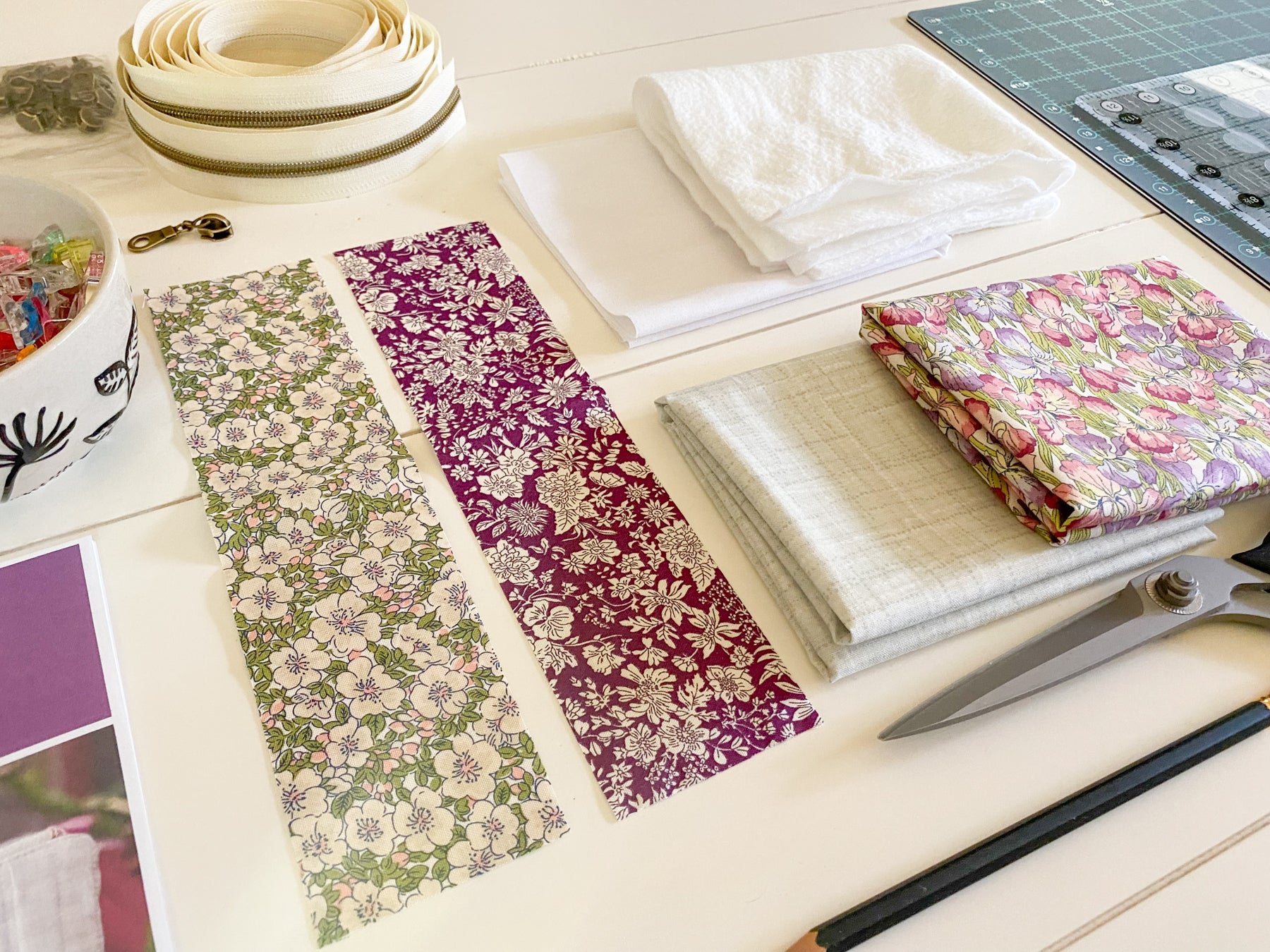 Cut fabric pieces for a zipper pouch laid out with sewing supplies, including scissors, a pencil, and a small jar of sewing clips—materials from the PDF sewing pattern