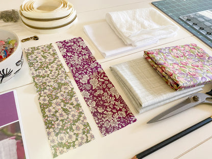 Cut fabric pieces for a zipper pouch laid out with sewing supplies, including scissors, a pencil, and a small jar of sewing clips—materials from the PDF sewing pattern