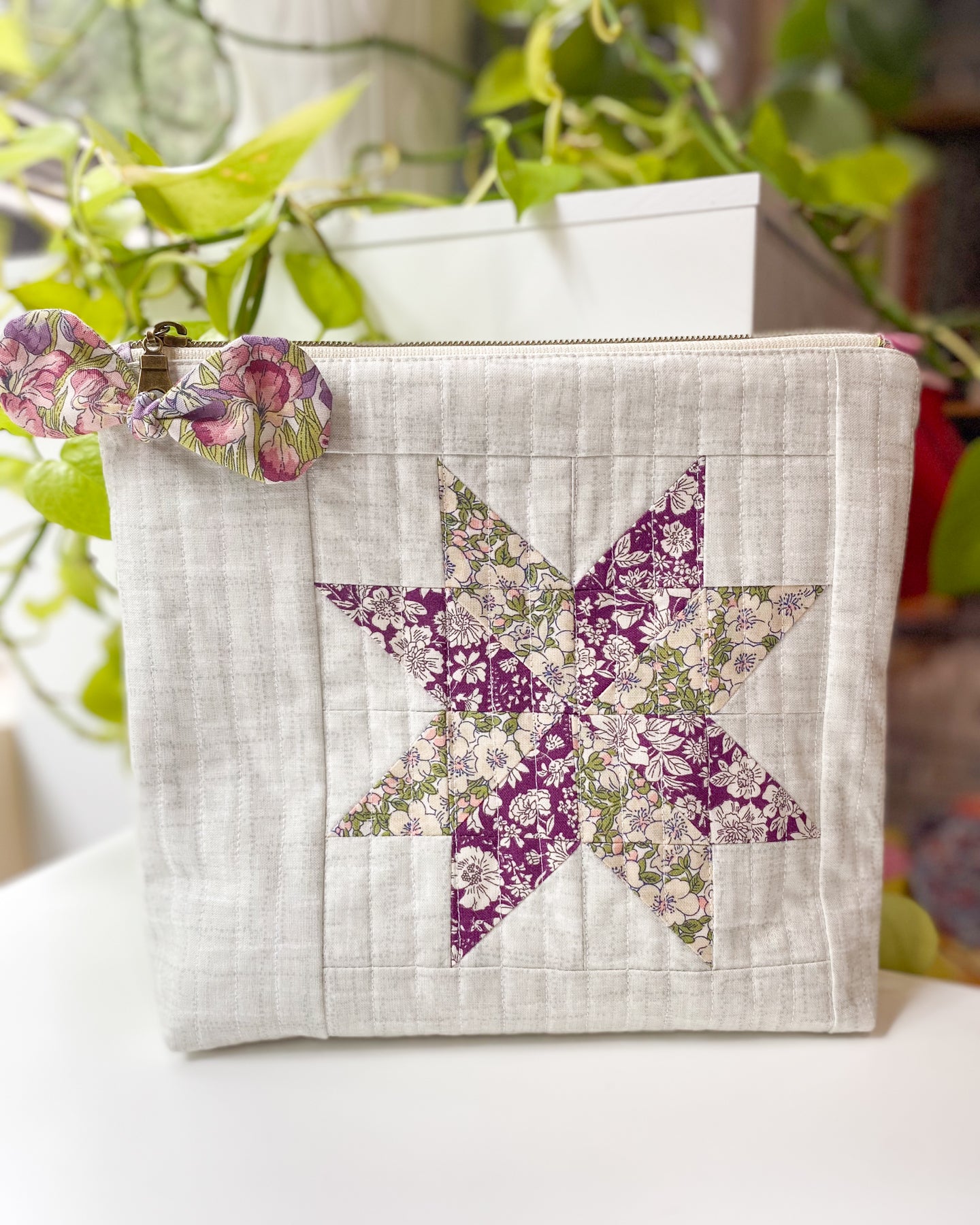 Zipper pouch made from PDF sewing pattern, featuring Liberty floral fabric and flat-bottom design, standing on a white table with greenery behind