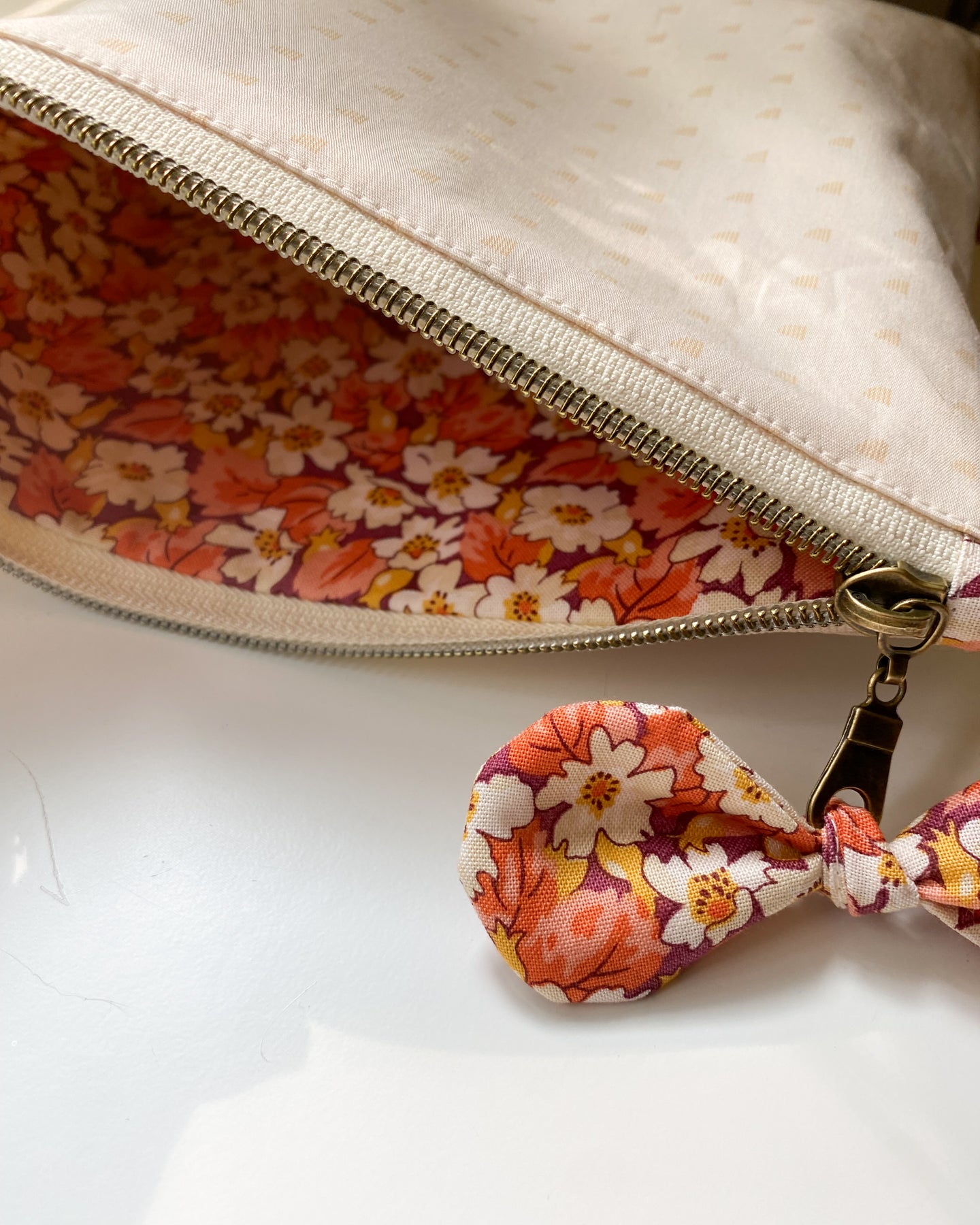 Zipper pouch laying flat and unzipped, showing matching floral fabric lining and a bow embellishment tied to the zipper pull