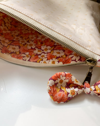 Zipper pouch laying flat and unzipped, showing matching floral fabric lining and a bow embellishment tied to the zipper pull