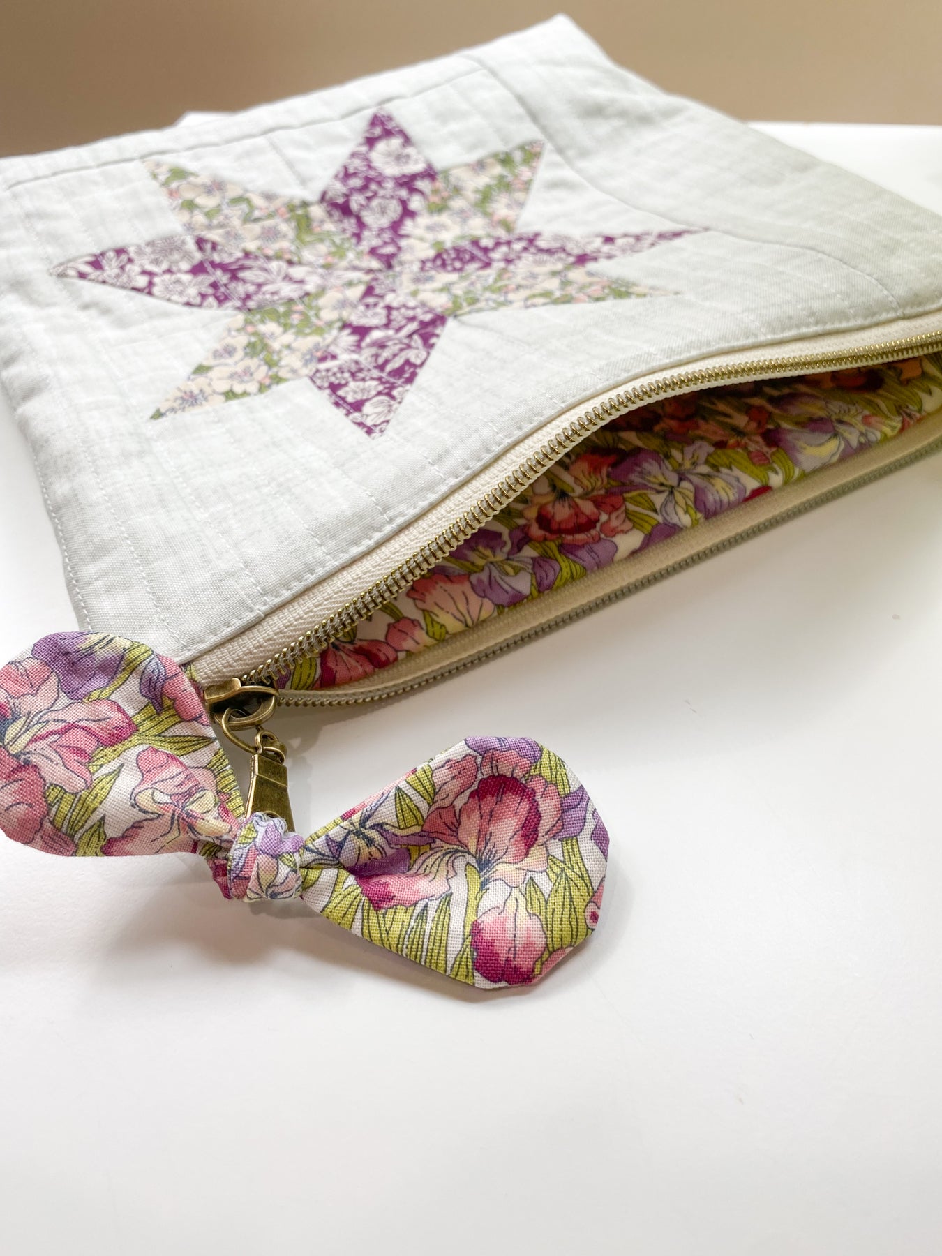 Zipper pouch laying flat and unzipped, showing matching floral fabric lining and a bow embellishment tied to the zipper pull